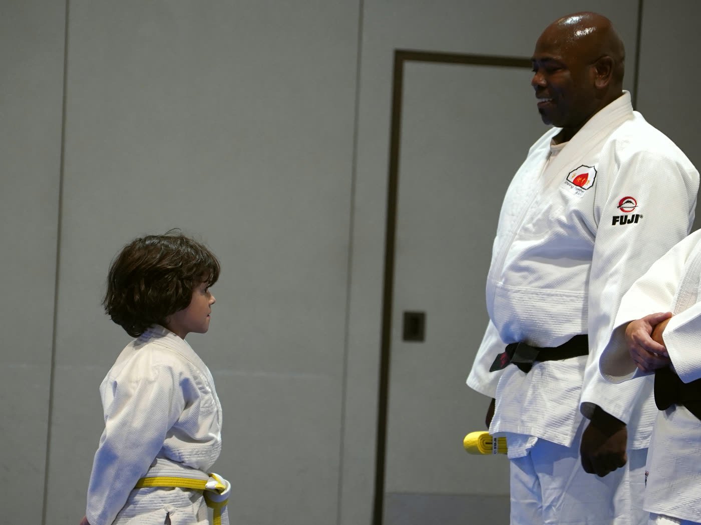 A young yellow-belt student looks up at Coach Dennis, who smiles down at him