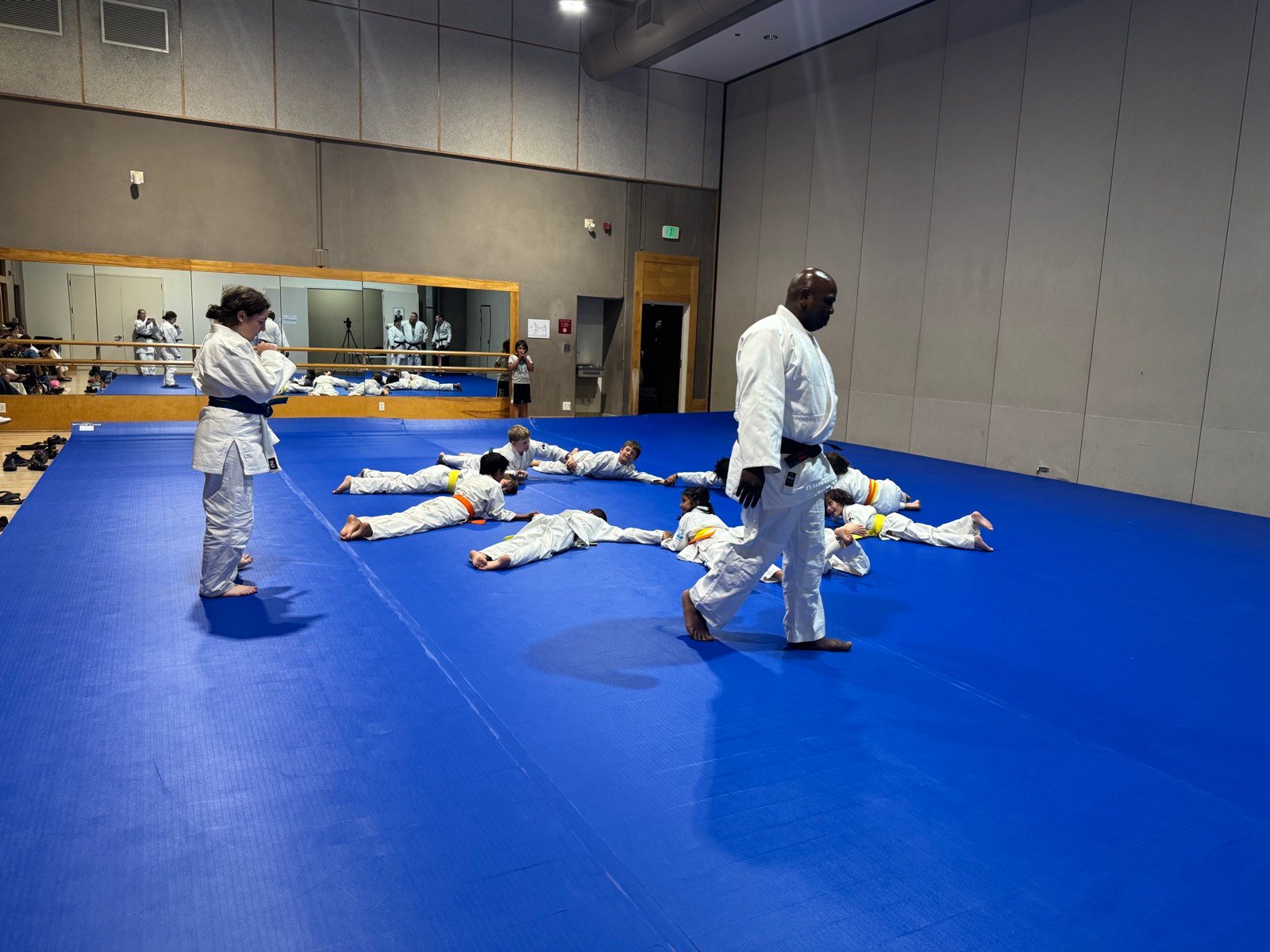 The class practising breakfalls on the blue mats at Finley Center while Coach Dennis watches