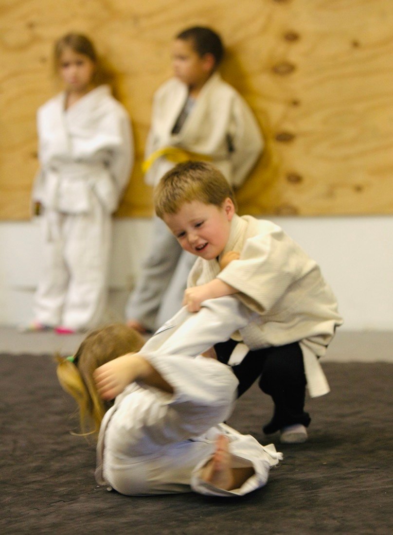 A grinning young boy throws a classmate onto the mat