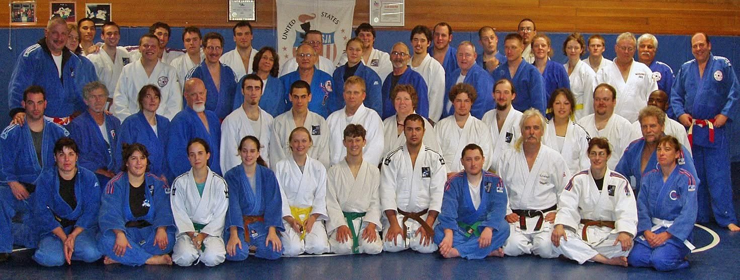 A large group of judoka in white and blue judogi posing together on the mat